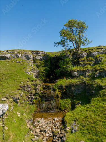 Waterfall and tree in Cray, Yorkshire Dales, UK. A gentle waterfall in the British countryside with a blue sky. photo