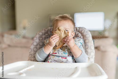 A boy being silly covering face while eating a sandwich