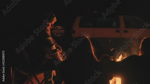 Goup of friends campers sits near the bonfire at night