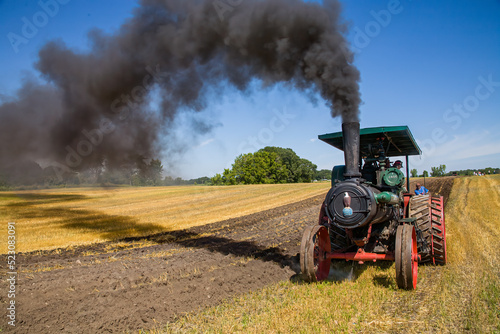 an old steam tractor with smoke billowing plows a farm field