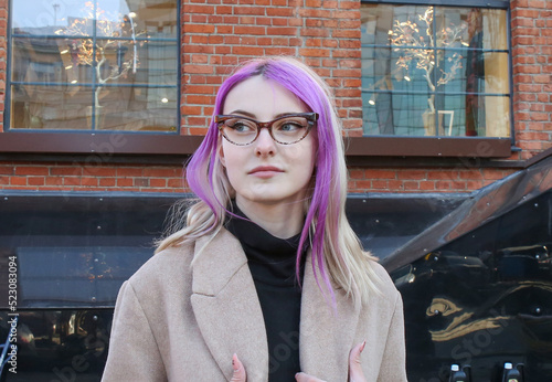 blonde with lilac strands of hair in a beige coat and glasses on the street
