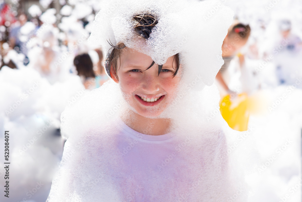 happy little boy with foam on his head, in wet clothes at a foam party or holiday on a sunny hot