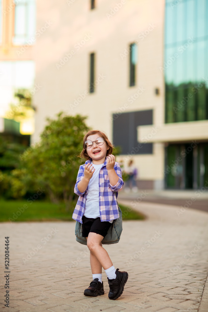 a little schoolgirl, standing in glasses,near the school building,with a backpack a little schoolgirl, standing in glasses,near the school building,with a backpack