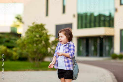 a little schoolgirl, standing in glasses,near the school building,with a backpack © khanfus
