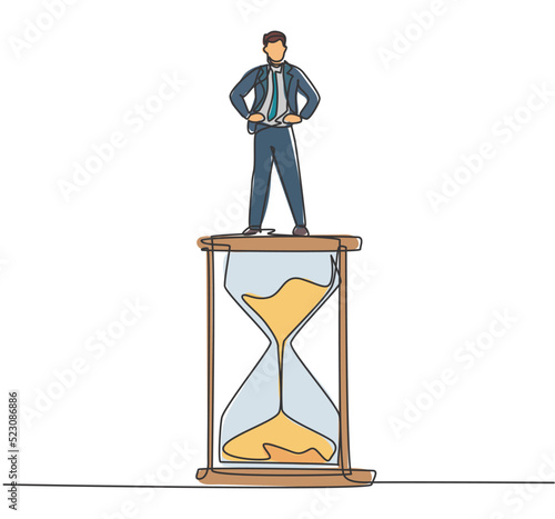 Continuous one line drawing young male worker standing above hourglass. Sandglass to show time management business minimalist concept. Single line draw design vector graphic illustration