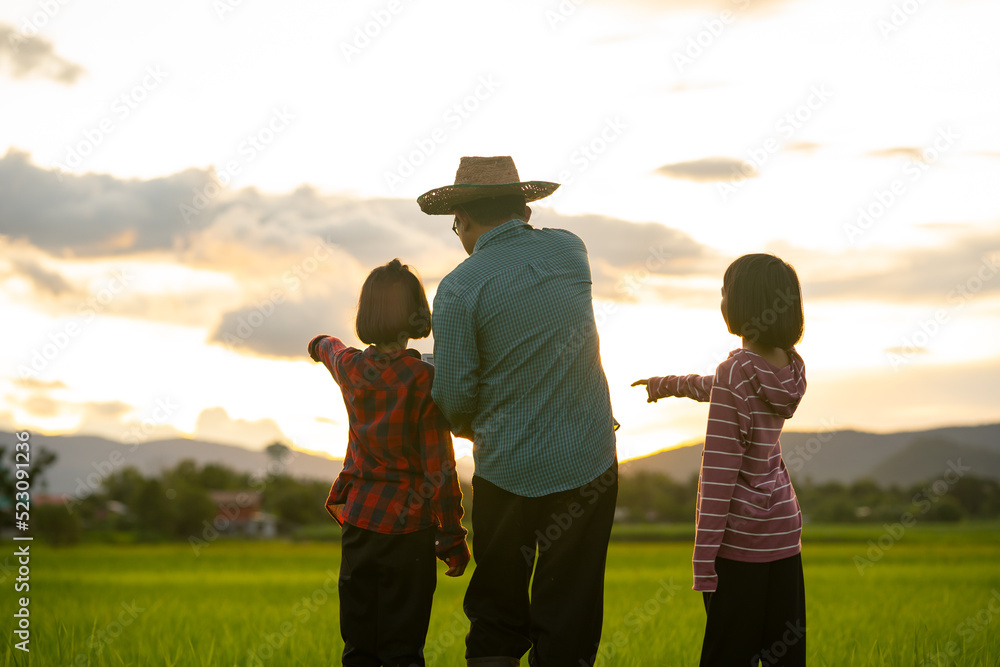 Fototapeta premium Father and children looking rice field and checking on laptop on sunset sky background