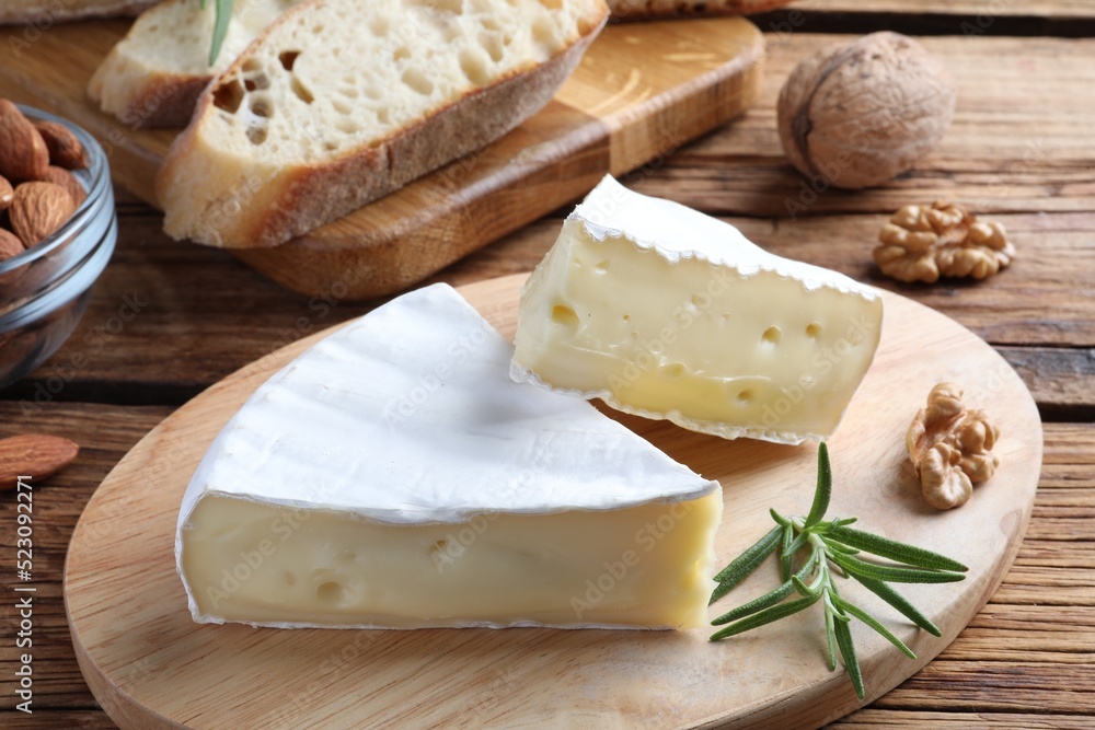 Tasty cut brie cheese with rosemary, bread and nuts on wooden table