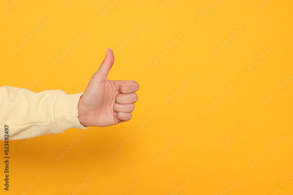 Woman showing thumb up on orange background, closeup. Space for text