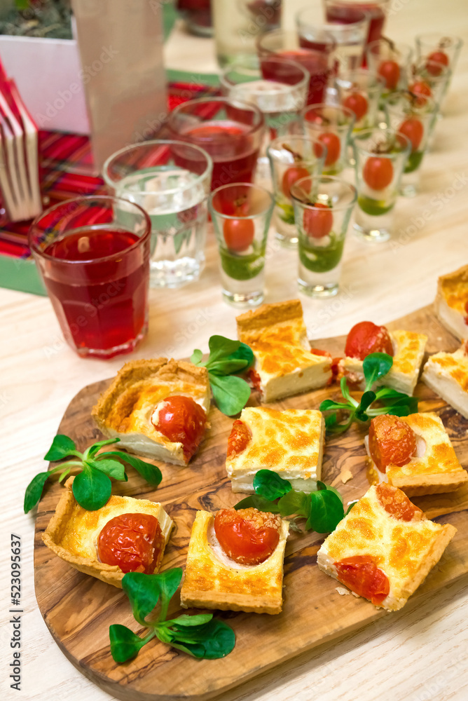 square slices of quiche with cherry tomatoes and corn lettuce leaves on a wooden cutting board, appetizer table with snacks and canapes