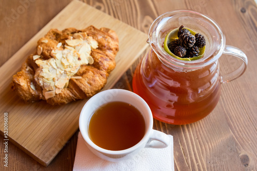 Breakfast in the cafe. juniper tea with lime served in a glass chemex, a cup of hot tea and a croissant with almonds.