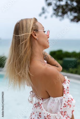 Tender soft romantic fashion portrait of tanned fit woman posing outdoor on sea background wearing sexy stylish dress and sunglasses