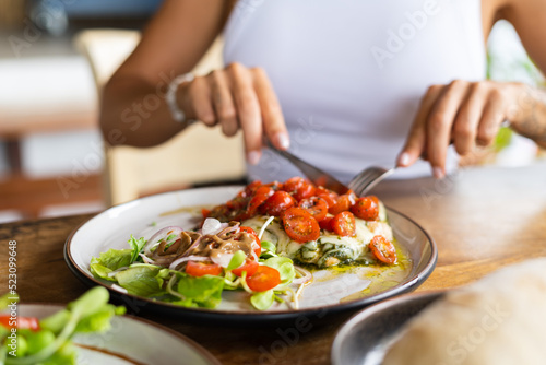 Woman having chicken pesto with cheese and tomatoes in summer cafe