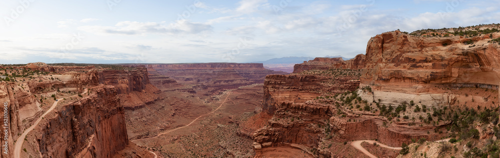 Scenic Dirt Road surrounded by Red Rock Mountains in Desert Canyon. Spring Season. Canyonlands National Park. Utah, United States. Adventure Travel. Panorama. Cloudy Sky Art Render