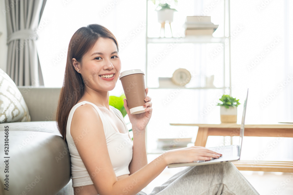 Freelance asian woman in glasses with mobile phone typing at laptop and working from home office. Happy girl sitting on couch in living room. Freelance asian woman in glasses with mobile phone typing at laptop and working from home office. Happy girl sitting on couch in living room.