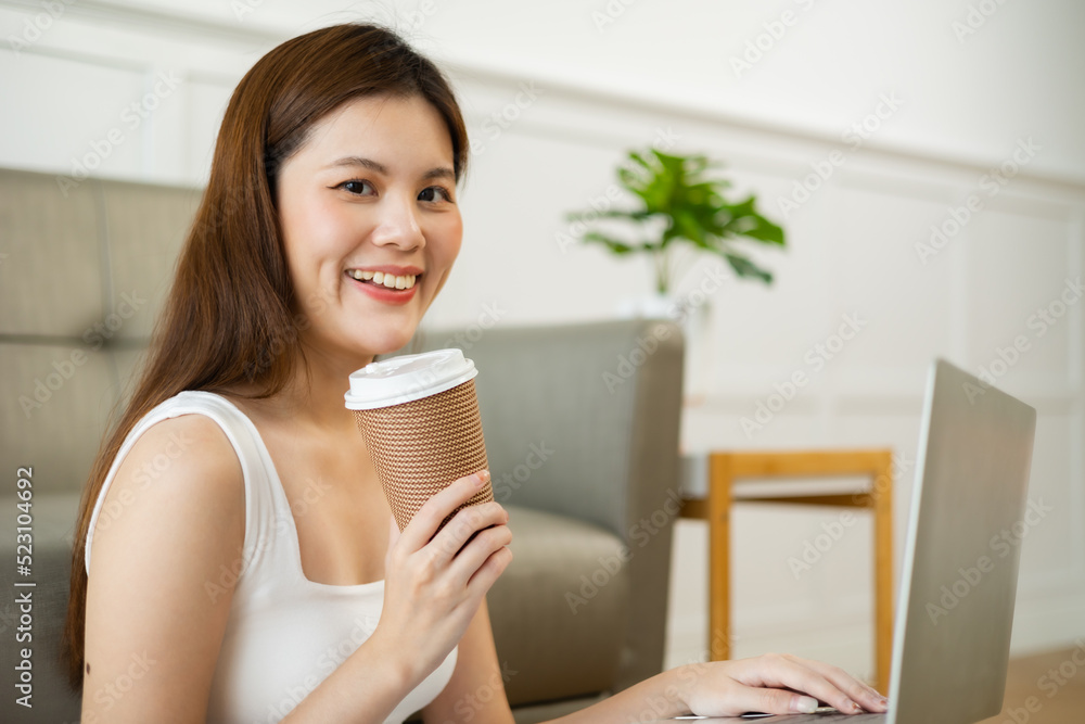 Freelance asian woman in glasses with mobile phone typing at laptop and working from home office. Happy girl sitting on couch in living room. Freelance asian woman in glasses with mobile phone typing at laptop and working from home office. Happy girl sitting on couch in living room.