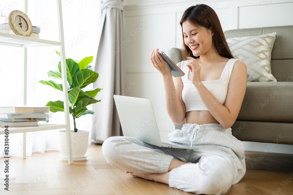 Freelance asian woman in glasses with mobile phone typing at laptop and working from home office. Happy girl sitting on couch in living room. Freelance asian woman in glasses with mobile phone typing at laptop and working from home office. Happy girl sitting on couch in living room.
