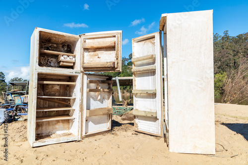 Photograph of a flood damaged refrigerators on a white sandy shore near the Hawkesbury river