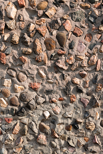 Texture of an old weathered concrete surface with red granite rubble in the structure.
