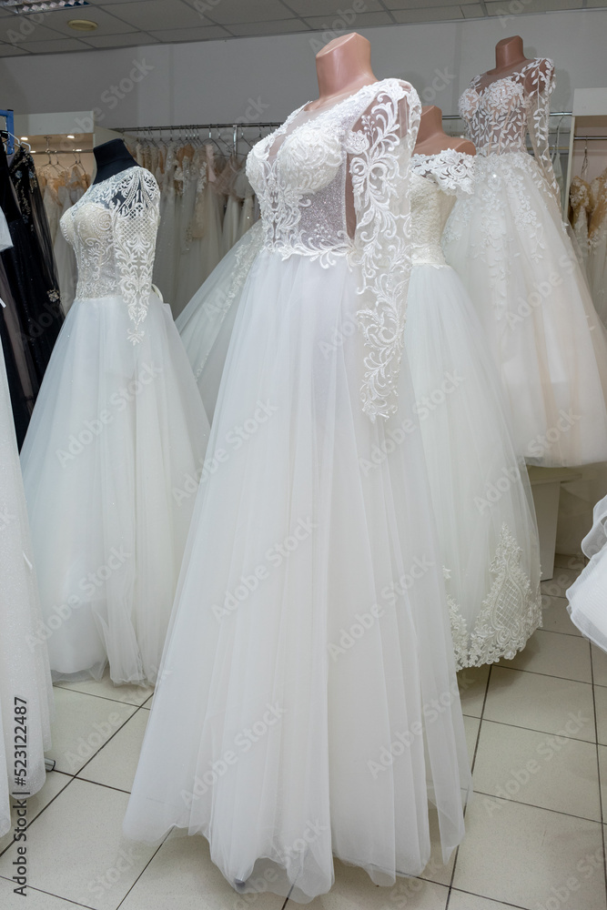 A beautiful white wedding dress on a mannequin. A close-up of a dress against other wedding dresses in a bridal shop A beautiful white wedding dress on a mannequin. A close-up of a dress against other wedding dresses in a bridal shop