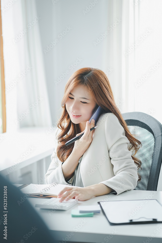 Female accountant using calculator and talking on telephone while sitting in an office. Female accountant using calculator and talking on telephone while sitting in an office.