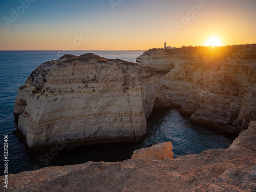 Limestone cliffs glow in the sunset over Alfanzina Lighthouse near Carvoeiro in Algarve, Portugal taken from the viewpoint near Floating Rock caves. Europe's most southerly Atlantic coastline. photo