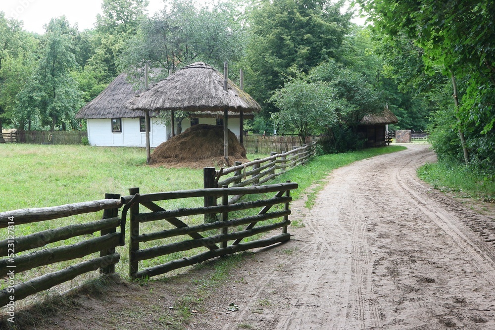 A dirt road that runs along the fence and the old thatched wooden farmhouse. A dirt road that runs along the fence and the old thatched wooden farmhouse.