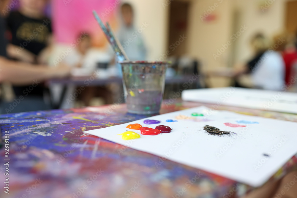 Paint brushes in glasses and colourful paints on white sheet of paper Paint brushes in glasses and colourful paints on white sheet of paper