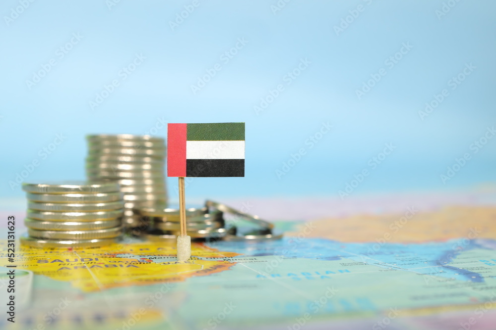 Selective focus of UAE flag in blurry world map with coins. UAE economy and wealth concept.