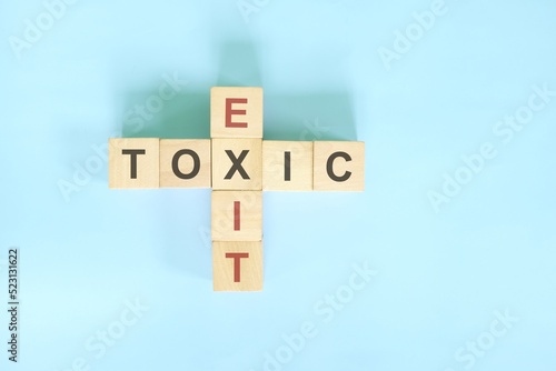 Resignation from toxic job, workplace or relationship concept. Exit and toxic wooden block crossword puzzle flat lay in blue background.