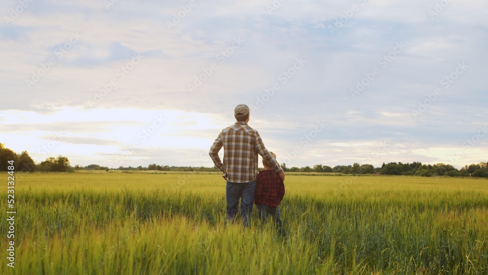 Farmer and his son in front of a sunset agricultural landscape. Man and a boy in a countryside field. Fatherhood, country life, farming and country lifestyle. Farmer and his son in front of a sunset agricultural landscape. Man and a boy in a countryside field. Fatherhood, country life, farming and country lifestyle.