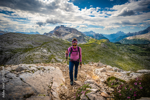 Young woman is hiking on beautiful trail with flowers from Baires Lake to Seekofel in the Dolomite mountains in the morning. Seekofel, Dolomites, South Tirol, Italy, Europe. © Michael