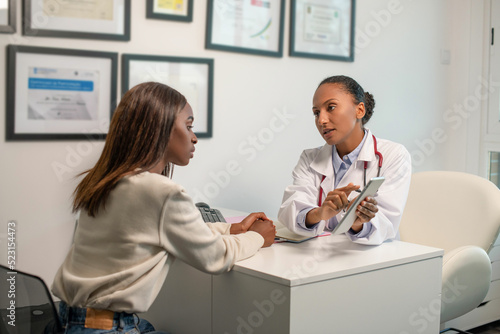 Confident doctor talking to patient and pointing at touchpad. Young African American woman having consultation in clinic. Medical consultation concept