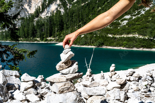Young woman builds stone man with Baires Lake in the background. Braies Lake Braies Lake (Pragser Wildsee, Lago di Braies), Dolomites, South Tirol, Italy, Europe. photo