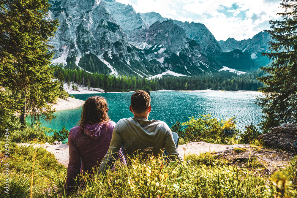 Young couple enjoys beautiful view on Baires Lake in the Dolomite mountains in the afternoon. Braies Lake (Pragser Wildsee, Lago di Braies), Dolomites, South Tirol, Italy, Europe.