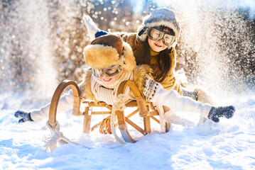 Two smiling children ride lying on a wooden retro sled on a sunny winter day. Active winter outdoors games. Happy Christmas vacation concept.