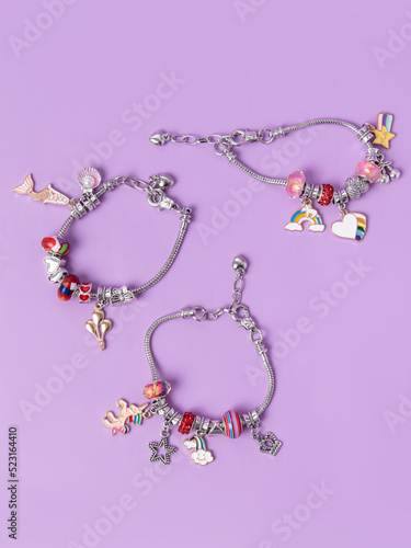 Three small silver charm bracelets with many charms on purple background. Creating jewelry. Children's bracelets