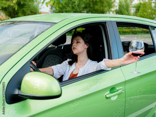 Young drunk girl driving a car with a glass of wine in her hand. Drinking alcohol while driving. a girl while driving a car stuck her hand out the window with a glass of wine