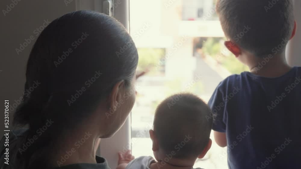 Back view of Mother and kids are looking out the window to the street and waving to somebody Back view of Mother and kids are looking out the window to the street and waving to somebody