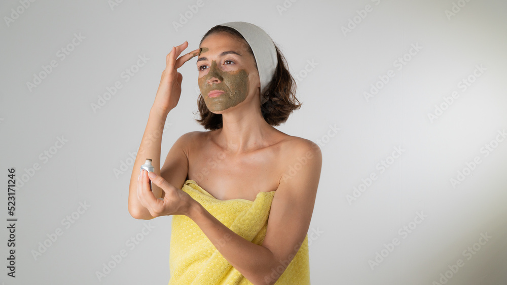 Fototapeta premium Woman in a towel makes a face mask - home care for the skin of the face
