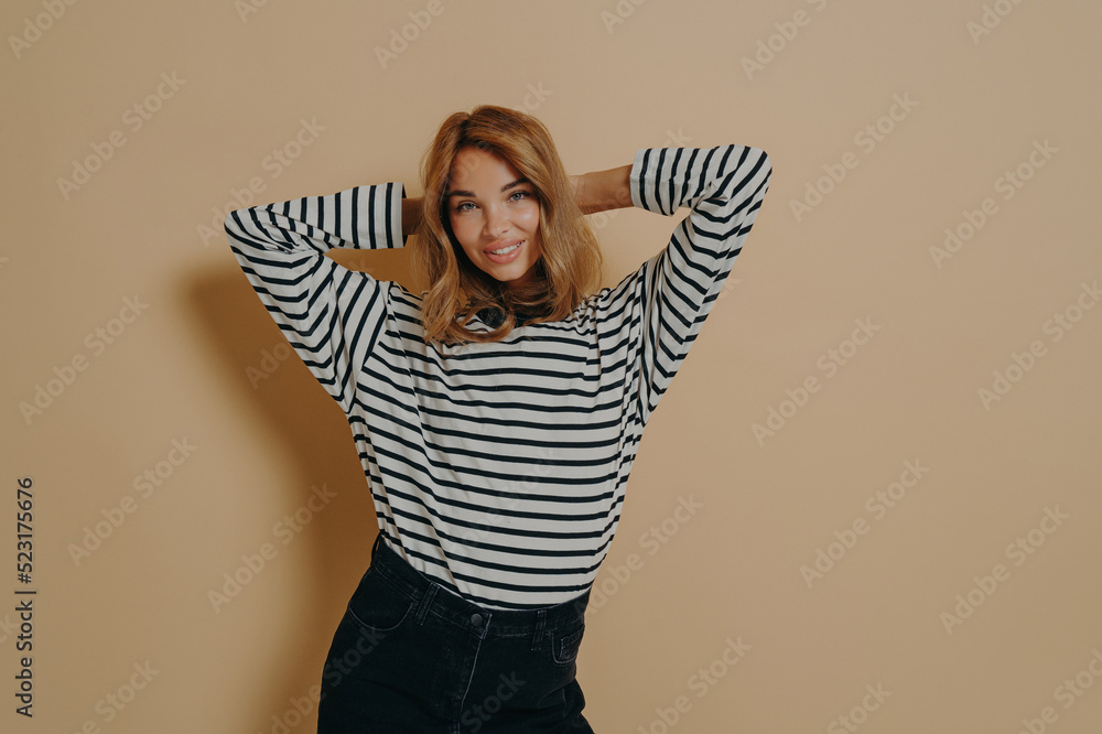 Half length shot of pretty satisfied young woman keeps hands behind head smiles gently poses indoor Half length shot of pretty satisfied young woman keeps hands behind head smiles gently poses indoor