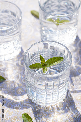 sprudelndes Wasser in einem durchsichtigen Glas mit einem Minzblatt auf einer gemusterten Tischdecke 
