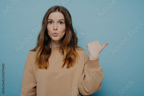 Surprised young woman pointing at copy space with wow expression