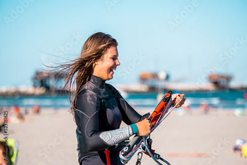 Beautiful kite surfing girl in pink bikini swimsuit adjusting kite surf on bright sunny day at ocean shore. Preparation before kiting. Watersport adrenaline fun adventure acitivity