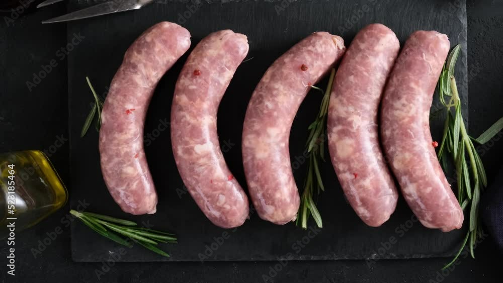 Oktoberfest food. Raw bratwurst or German pork sausages with rosemary and spices on dark background. Top view. 4k video Oktoberfest food. Raw bratwurst or German pork sausages with rosemary and spices on dark background. Top view. 4k video