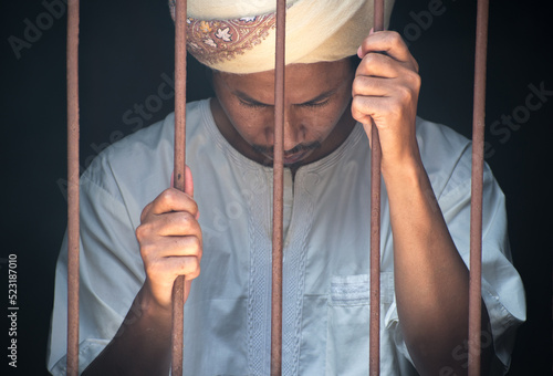 Religious muslim islam man in white session hold steel in jail on black background, concept for prisoner,sadness,detain,erroneousness