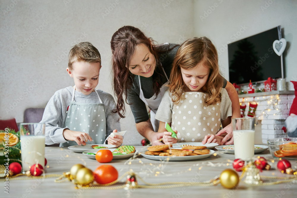 Mother, daughter and son is cooking Christmas cookies. Family is preparing holiday food. Funny Christmas time and holidays. Two glasses of milk on the table for Santa. Mother, daughter and son is cooking Christmas cookies. Family is preparing holiday food. Funny Christmas time and holidays. Two glasses of milk on the table for Santa.