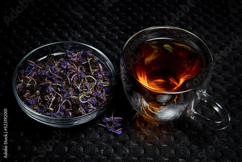 Homemade natural fermented tea with inclusions of blue Chamaenérion angustifolium flowers in a glass bowl on a black background next to a glass of tea.