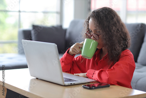 Smart and active latin woman sitting on sofa and using internet on computer with smart mobile phone while drinking coffee in living room. Lifestyle with technology