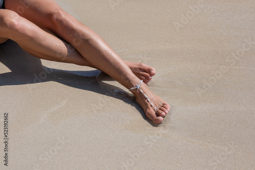 Girl sunbaths on the beach wearing an anklet