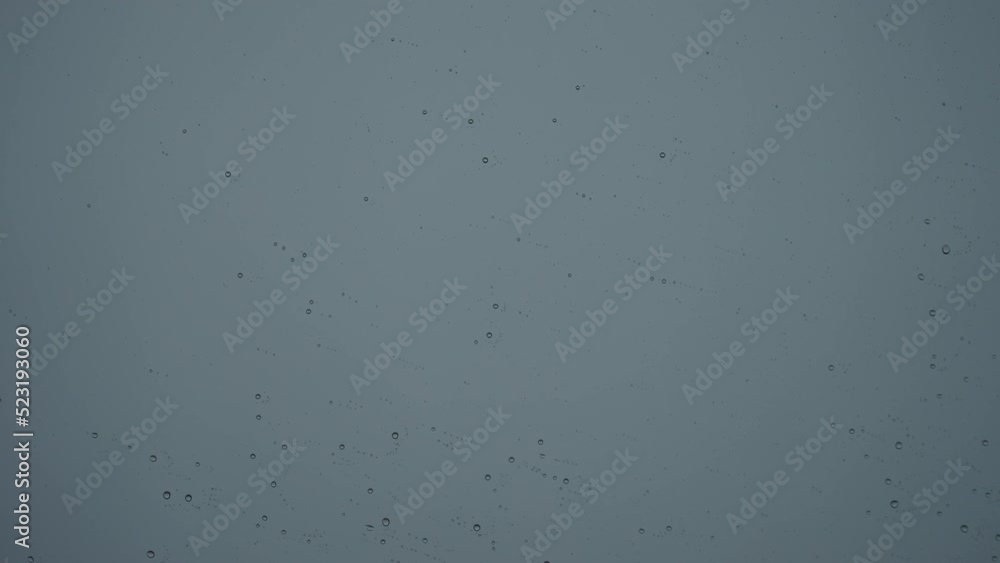 Slow motion raindrops on window glass with storm clouds on background Slow motion raindrops on window glass with storm clouds on background